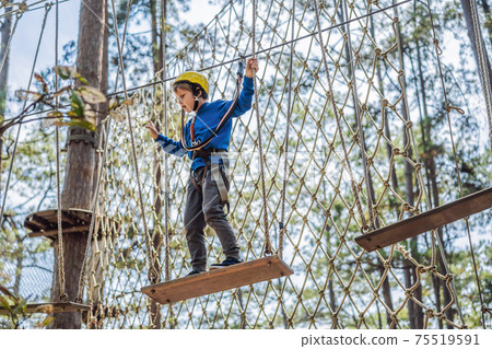 Happy child in a helmet, healthy teenager school boy enjoying activity in a climbing adventure park on a summer day Happy child in a helmet, healthy teenager school boy enjoying activity in a climbing adventure park on a summer day 75519591