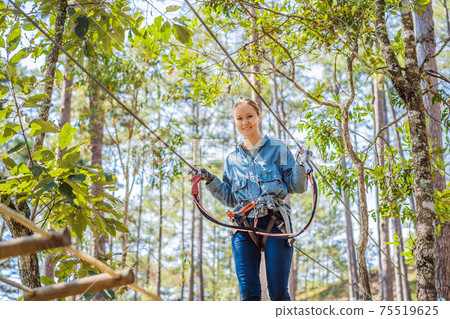 Young brave woman climbing in a adventure rope park Young brave woman climbing in a adventure rope park 75519625