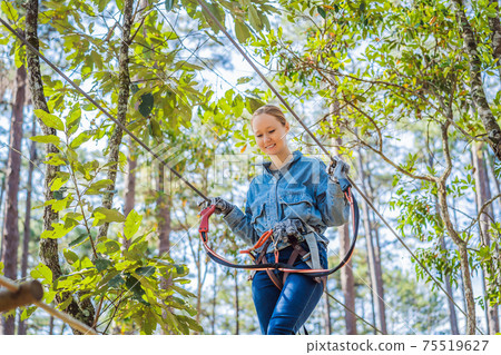 Young brave woman climbing in a adventure rope park 75519627