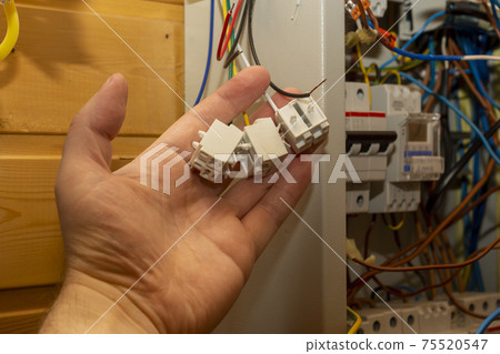 Hand holds electrical connectors by a large electrical panel indoors 75520547