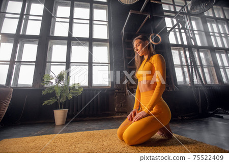 a beautiful girl in a yellow tracksuit does stretching. Modern sports hall with large windows a beautiful girl in a yellow tracksuit does stretching. Modern sports hall with large windows 75522409
