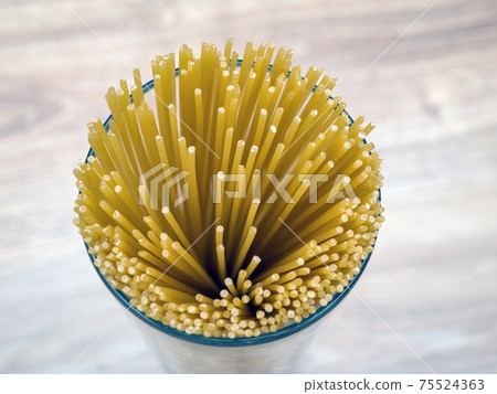 Uncooked spaghetti in glass vase on a wooden background. Close-up. Uncooked spaghetti in glass vase on a wooden background. Close-up. 75524363