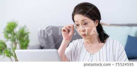 Presbyopia: Banner size of a senior woman who looks at a computer with reading glasses without seeing the screen well Presbyopia: Banner size of a senior woman who looks at a computer with reading glasses without seeing the screen well 75524595