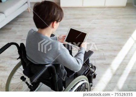 Handicapped teenage boy in wheelchair holding tablet with blank screen indoors, mockup for website or app design Handicapped teenage boy in wheelchair holding tablet with blank screen indoors, mockup for website or app design 75526355