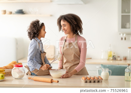 Happy black woman and daughter kneading dough in kitchen Happy black woman and daughter kneading dough in kitchen 75526961