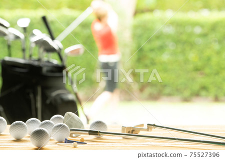Golf balls, golf equipment and golf club on the table on driving range with the golfer in background Golf balls, golf equipment and golf club on the table on driving range with the golfer in background 75527396