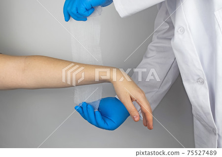The traumatologist puts a bandage on the forearm of the female patient. The concept of help with fractures and sprains. The technique of applying a cruciform bandage. The traumatologist puts a bandage on the forearm of the female patient. The concept of help with fractures and sprains. The technique of applying a cruciform bandage. 75527489