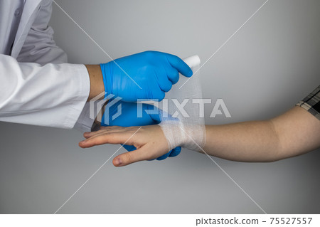 The traumatologist applies a bandage to the patient's wrist. The concept of helping with fractures and sprains. The technique of applying a cruciform bandage. 75527557