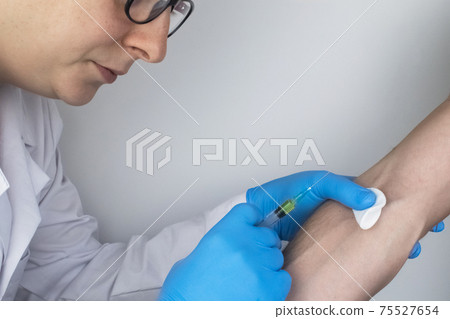 A doctor in blue medical gloves makes an injection into a vein. Intravenous drug administration. The concept of providing professional medical care A doctor in blue medical gloves makes an injection into a vein. Intravenous drug administration. The concept of providing professional medical care 75527654