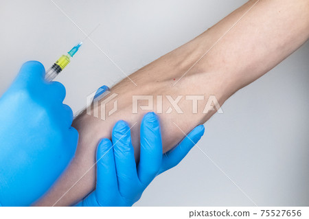 A doctor in blue medical gloves makes an injection into a vein. Intravenous drug administration. The concept of providing professional medical care 75527656