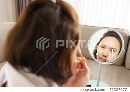 Young beautiful asian woman applying make up front a mirror at home. painting cosmetics for perfect skin and Make up in process concept. Young beautiful asian woman applying make up front a mirror at home. painting cosmetics for perfect skin and Make up in process concept. 75527677