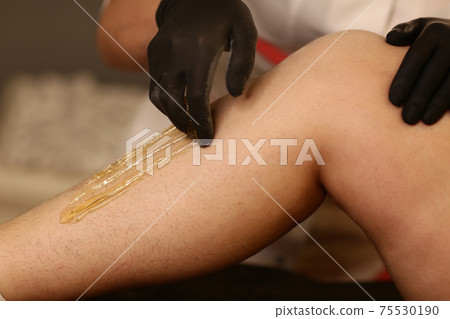 cosmetician hands make depilation procedure on woman legs with wax 75530190