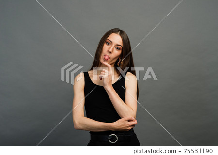 Cheerful young beautiful girl smiling winking showing tongue looking at camera over grey background. Emotional. Cheerful young beautiful girl smiling winking showing tongue looking at camera over grey background. Emotional. 75531190