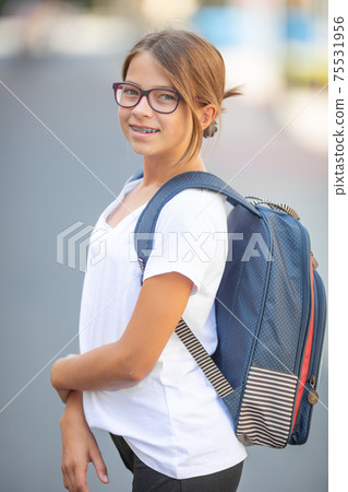 Young teenage in glasses and braces girl wears rucksack and a white t-shirt Young teenage in glasses and braces girl wears rucksack and a white t-shirt 75531956