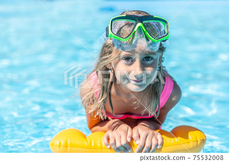 Young girl rests on floating pillow inside the pool with swimming goggles on her forehead, smiling Young girl rests on floating pillow inside the pool with swimming goggles on her forehead, smiling 75532008