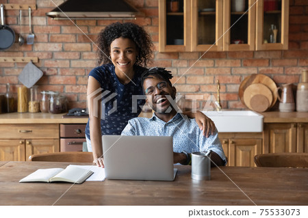 Happy modern day african family couple using laptop at kitchen 75533073