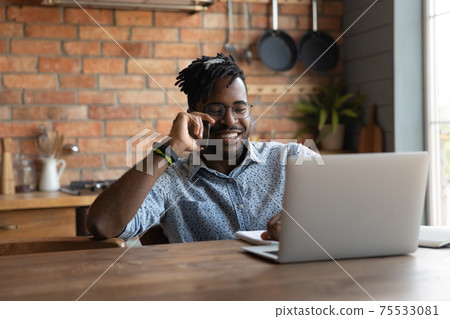 Positive african man answer phone call reading data on laptop Positive african man answer phone call reading data on laptop 75533081