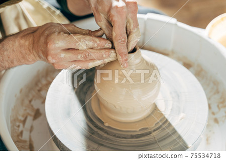Skilled wet hands of potter shaping the clay on potter wheel 75534718