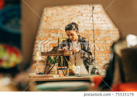 Girl in plaid shirt standing at her loft studio and making wonderful mosaic 75535179