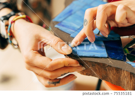 Young girl sitting and holding a tweezers, while making a mosaic 75535181