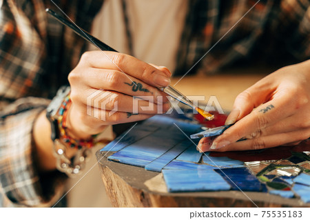 Women's hands collect colored pieces of smalt mosaic while putting the clue 75535183