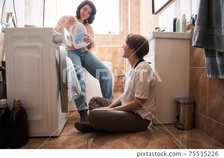 Lesbian couple doing laundry together at home at the bathroom Lesbian couple doing laundry together at home at the bathroom 75535226