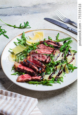 Beef steak tagliata with arugula and parmesan on gray plate, gray background. Italian cuisine concept. 75535418