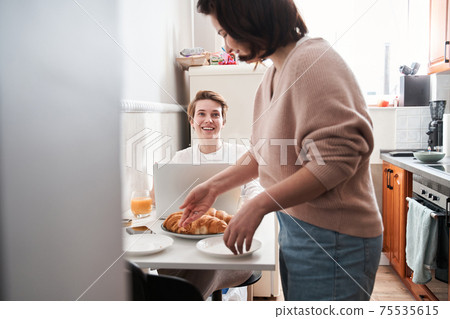 Girl cleaning the table after breakfast while chatting with her girlfriend Girl cleaning the table after breakfast while chatting with her girlfriend 75535615