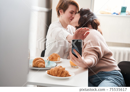 Woman hiding camera of the smartphone while kissing and making selfie Woman hiding camera of the smartphone while kissing and making selfie 75535617
