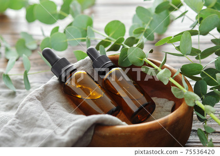 Two bottles of eucalyptus essential oil in wooden bowl and eucalyptus twigs on table. Two bottles of eucalyptus essential oil in wooden bowl and eucalyptus twigs on table. 75536420