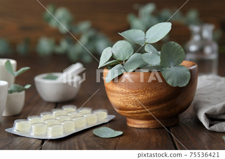 Wooden mortar of green eucalyptus leaves and lozengers for care sore throat and cough. Wooden mortar of green eucalyptus leaves and lozengers for care sore throat and cough. 75536421