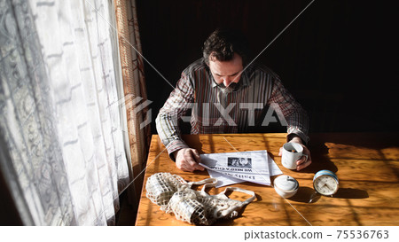 Portrait of unhappy poor mature man reading newspapers indoors at home, poverty concept. Portrait of unhappy poor mature man reading newspapers indoors at home, poverty concept. 75536763
