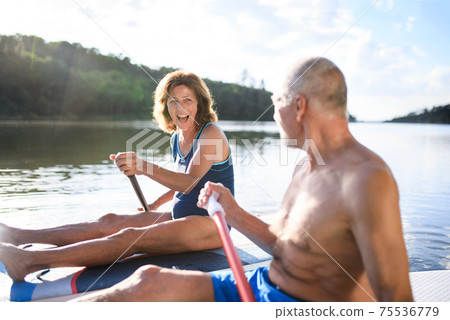 Senior couple paddleboarding on lake in summer. Senior couple paddleboarding on lake in summer. 75536779
