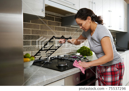 Young brunette woman cleans the surface of the stove. Homework and houselife concept 75537296