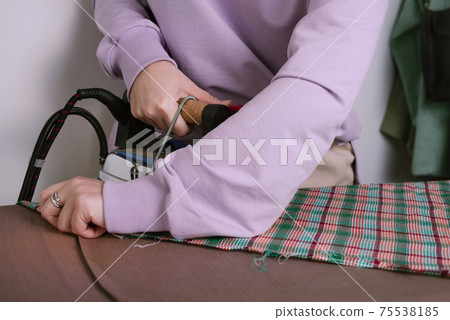 Closeup of female ironing plaid fabric in sewing workshop Closeup of female ironing plaid fabric in sewing workshop 75538185