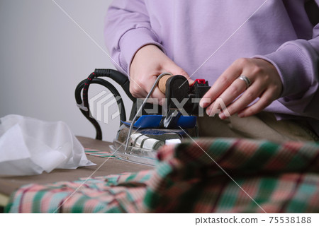 Closeup of female ironing plaid fabric in sewing workshop Closeup of female ironing plaid fabric in sewing workshop 75538188