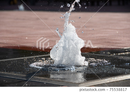 A small fountain on the street corner in early summer 75538817