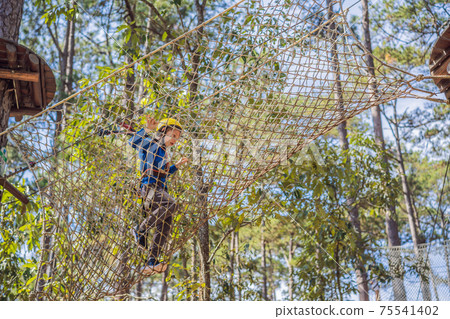 Happy child in a helmet, healthy teenager school boy enjoying activity in a climbing adventure park on a summer day 75541402