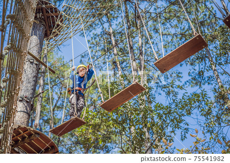 Happy child in a helmet, healthy teenager school boy enjoying activity in a climbing adventure park on a summer day 75541982