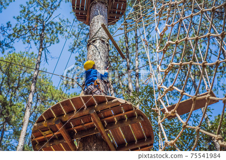 Happy child in a helmet, healthy teenager school boy enjoying activity in a climbing adventure park on a summer day 75541984