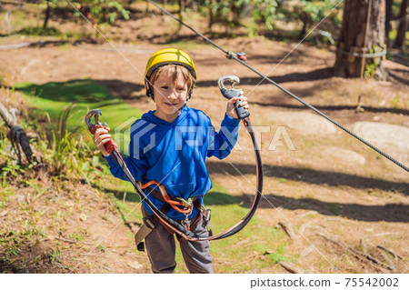 Happy child in a helmet, healthy teenager school boy enjoying activity in a climbing adventure park on a summer day 75542002