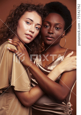 two pretty girls african and caucasian blond posing cheerful together on brown background, ethnicity diverse lifestyle people concept 75542762