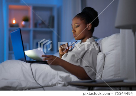woman with laptop working in bed at night woman with laptop working in bed at night 75544494