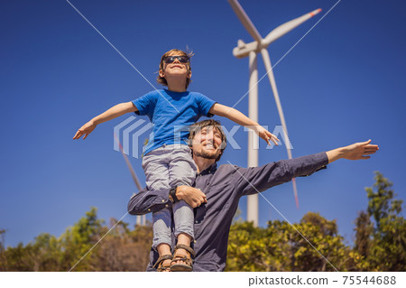 Alternative energy, wind farm and happy time with your family. Happy father carrying his son on shoulders is on vacation and escape to nature. Father carrying son on shoulders and waving their arms 75544688