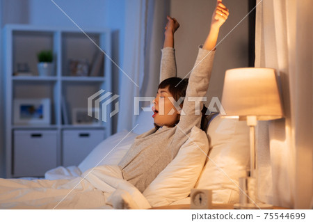 tired asian woman stretching in bed at night 75544699