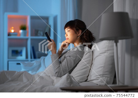 asian woman with smartphone in bed at night 75544772
