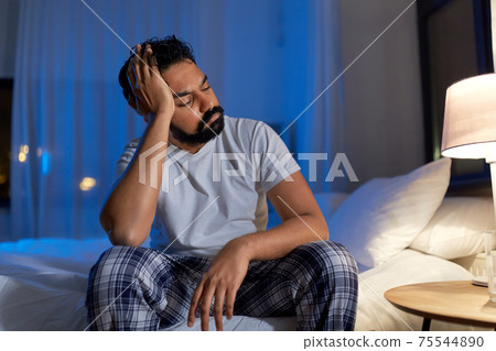 stressed indian man sitting on bed at night stressed indian man sitting on bed at night 75544890
