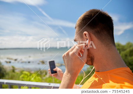 young man with smartphone and earphones outdoors 75545245