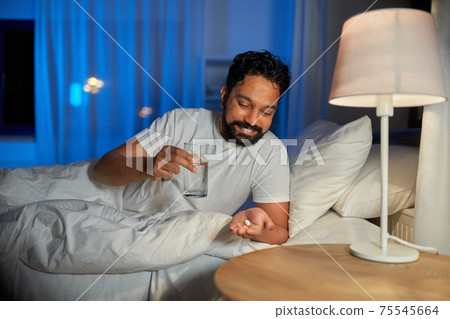 indian man with medicine and water in bed at night indian man with medicine and water in bed at night 75545664