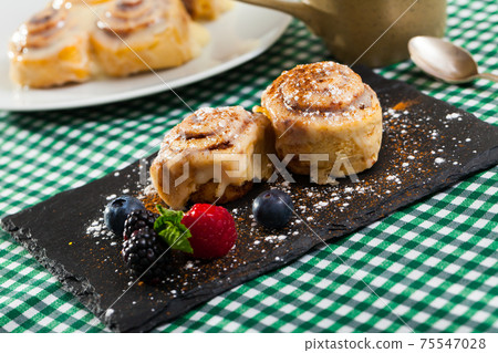 Tasty cinnamon rolls with fresh berries and powdered sugar at plate Tasty cinnamon rolls with fresh berries and powdered sugar at plate 75547028